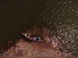 Cena do filme O Pescador e o Rio, baseado na lenda do Cabeça de Cuia. Imagem vista de cima. Mostra uma mulher com um vestido azul sentada em uma canoa nas margens de um rio.