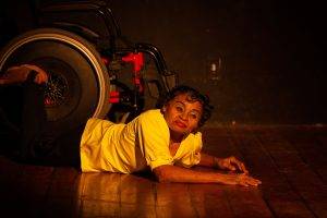 Foto de uma mulher dançando, ela está deitada no chão. Tem o cabelo curto e usa um batom vermelho.