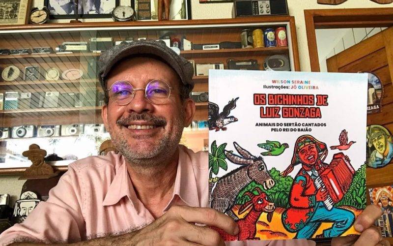 Foto de Wilson Seraine sorrindo e segurando o livro dele Os bichinhos de Luiz Gonzaga.