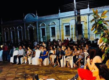 Foto da praça à noite cheia de pessoas sentadas assistindo às apresentações.