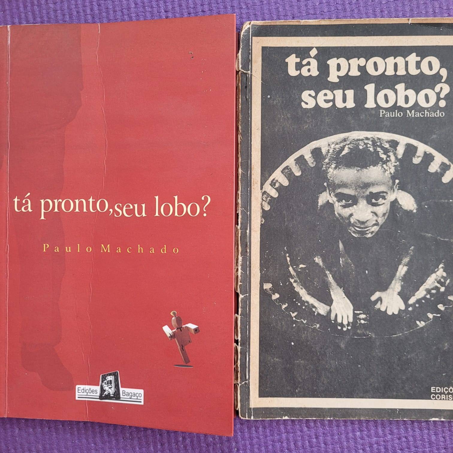 Foto do livro Tá pronto, seu lobo? de Paulo Machado. Sobre um tecido roxo há a primeira e a segunda edição do livro.