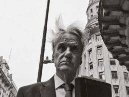 Foto em preto e branco de um senhor de terno com o cabelo bagunçado pelo vento. Ao fundo, a fachada de alguns prédios. Obra do fotógrafo piauiense Adriano Carvalho, premiada no IPPAWARDS.